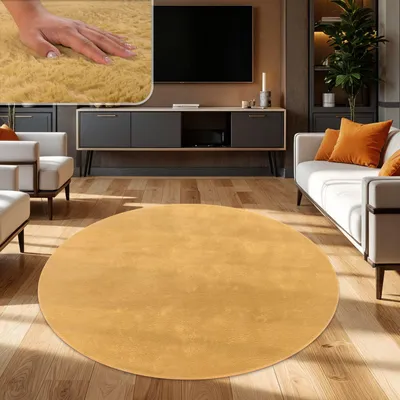 A round, yellow rug is placed on a wooden floor in a modern living room with a sofa and entertainment center.