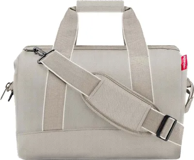 A studio shot of a beige duffel bag with a shoulder strap.
