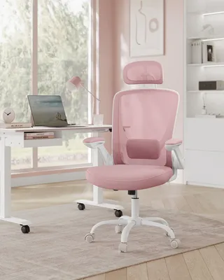 A pink ergonomic office chair is placed next to a white desk with a laptop in a bright, modern room with large windows.