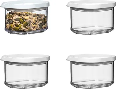 Four clear storage containers with white lids are arranged in a two-by-two grid on a white background. One container is filled with seeds.