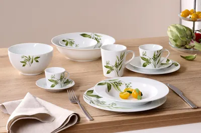 A set of white ceramic tableware with a green leaf pattern, arranged on a wooden table.