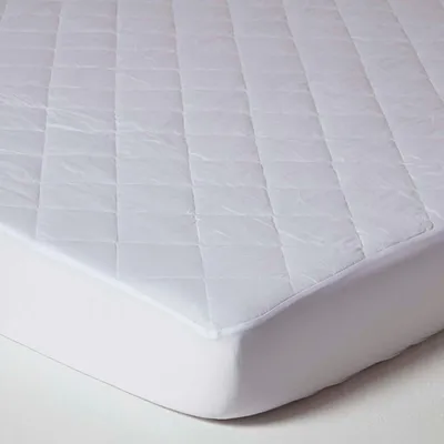A close-up view of a white quilted mattress protector with a fitted elastic edge.