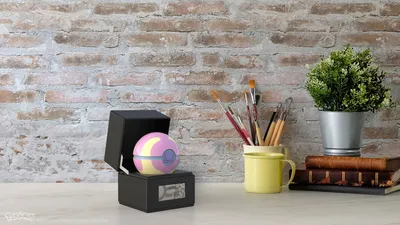 A Pokémon Heilball is displayed in an open black box on a white desk, with a brick wall background.