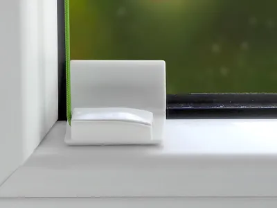 A close-up view of a white plastic mounting bracket with a green cord attached, placed on a white windowsill next to a window frame.