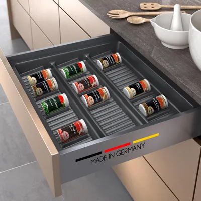 A kitchen drawer organizer filled with spice jars, with kitchen utensils and bowls on the counter.