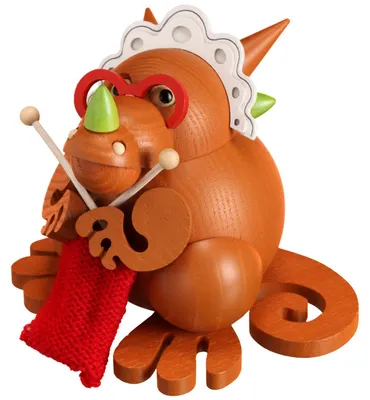 Ein orangefarbener Drache aus Holz mit Brille und Haube strickt mit zwei Nadeln an einem roten Wollstück und sitzt dabei auf einem runden Sockel