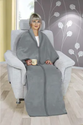 A woman sits in a chair wrapped in a grey blanket, holding a mug.