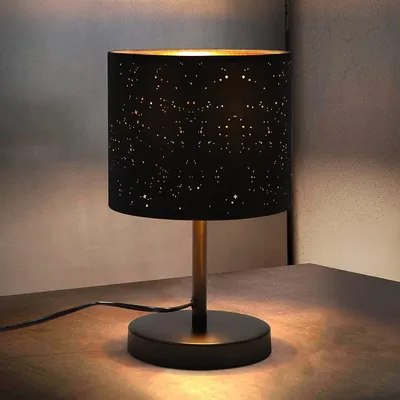 A black table lamp with a star pattern on the lampshade sits on a wooden surface.