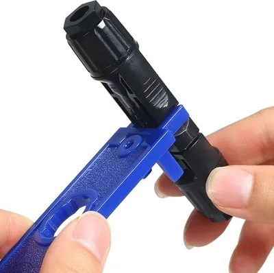 A hand is holding a blue tool to connect a black solar connector.