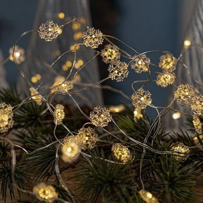 A close-up shot of a string of snowflake-shaped LED lights intertwined with green pine branches.