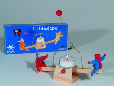A wooden candle-powered mobile toy with figures on a seesaw, next to its packaging.