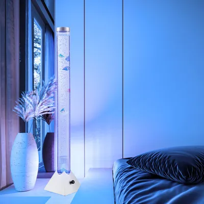 A bubble lamp with decorative fish is placed next to a window and a bed in a room with blue lighting.