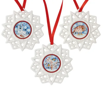 Three white ceramic star-shaped ornaments with painted scenes in the center, hanging from red ribbons.
