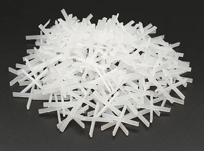 A pile of white tile spacers on a black background.