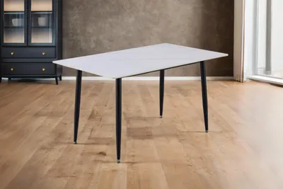 A rectangular dining table with a white marble-like top and black legs is shown in a room with wooden floors and a dark cabinet in the background.