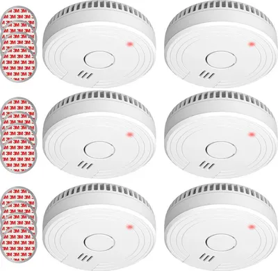 A set of six smoke detectors arranged in a grid on a white background, with adhesive pads to the left.