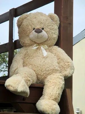 A large teddy bear sitting on wooden steps outdoors.