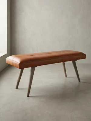 Freigestellte Frontansicht der Retro-Stil Bank. Gepolsterte Echtlederbank in Braun mit ausgestellten Beinen aus massivem Mangoholz, perfekt als stilvolle Dielenmöbel oder Bettbank._#sku_SAFWL5.319#