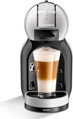 A black and silver Krups Mini Me coffee machine with a glass of latte macchiato.