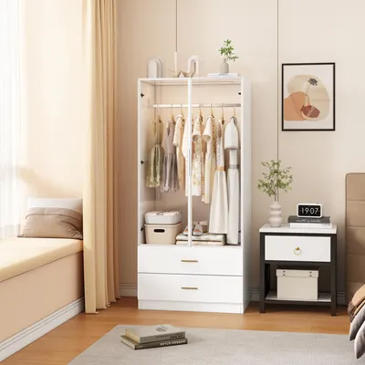 A bedroom scene with a white wardrobe, a nightstand, and a bed. The wardrobe is open, showing clothes on hangers and drawers. A window with curtains is visible on the left.
