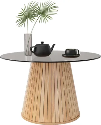 A round glass-top table with a wooden base, featuring a black teapot and cup, and a vase with green leaves.