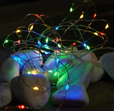 A string of colorful LED lights is draped over smooth, light-colored stones.