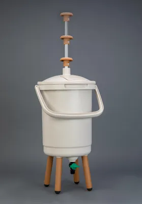 A beige Bokashi composter with a green spigot and brown legs, set against a plain gray background.