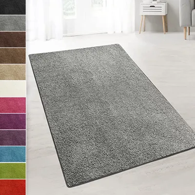 A gray shaggy rug is laid out on a light-colored floor in a room with white curtains and a white side table.