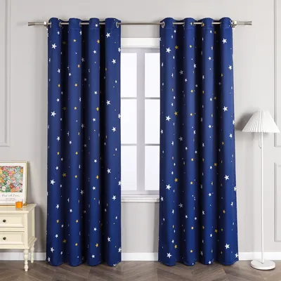 Two blue curtains with white and yellow stars are hanging in front of a window. A white nightstand with a framed picture and a small orange candle is to the left of the curtains. A white floor lamp is to the right.