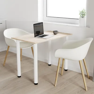 A small dining table with two chairs in a bright, modern room setting, with a laptop and a mug on the table.