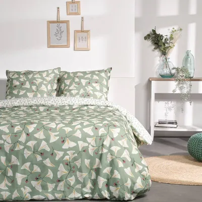 A bedroom scene with a bed made up with a green duvet cover set featuring a leaf pattern. There are framed pictures on the wall and a shelf with decorative items.