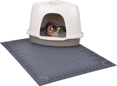 A cat is inside a litter box that is placed on a litter mat.