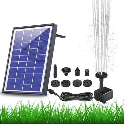 A solar-powered fountain pump kit is displayed on a white background with green grass at the bottom. The kit includes a solar panel, a pump with a water jet, and various nozzle attachments.