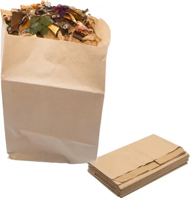 A brown paper bag filled with compostable material and a stack of brown paper bags next to it.
