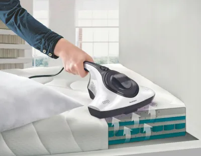 A person is using a handheld vacuum cleaner on a mattress.