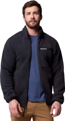 A man wearing a black fleece jacket and a blue t-shirt, standing against a white background.