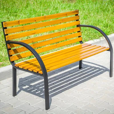 A wooden and metal park bench sits on a paved walkway next to a grassy area.