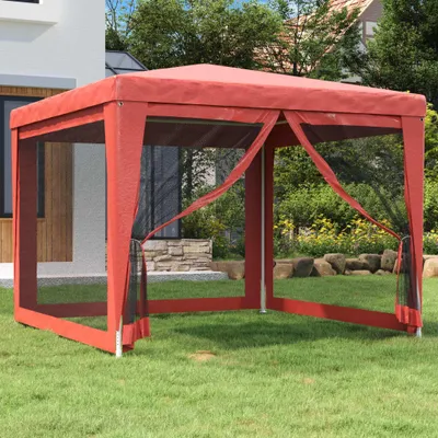 A red party tent with mesh sides is set up on a green lawn in front of a house and trees.