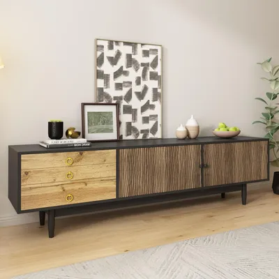 A modern TV stand with a black top and base, featuring three wooden drawers on the left and two wooden doors with a textured pattern on the right. It is decorated with artwork, a plant, and decorative items.