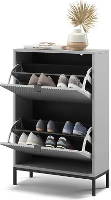 A gray shoe cabinet with two flip-down drawers, filled with shoes, is shown against a white background. A decorative plant in a vase sits on top of the cabinet.