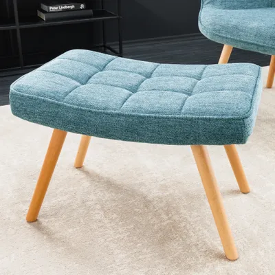 A blue upholstered ottoman with wooden legs sits on a light-colored rug, with a bookshelf in the background.