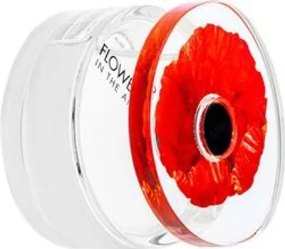 A close-up view of a perfume bottle cap with a red poppy flower embedded within it.