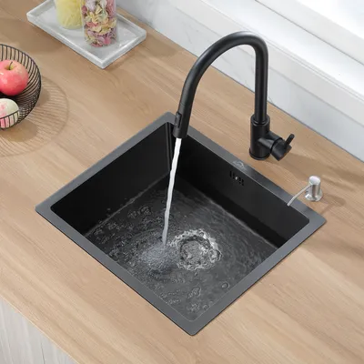 A black kitchen sink with water running from a black faucet, set into a wooden countertop. A soap dispenser is also visible.