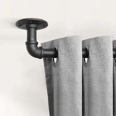 A close-up view of a black metal pipe curtain rod bracket mounted on a white ceiling, holding gray curtains.