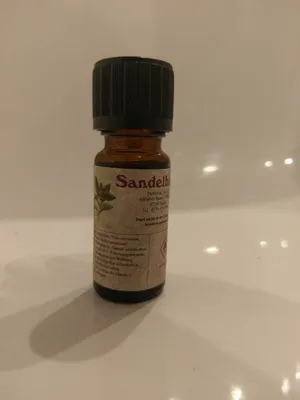 Kleine braune Flasche mit einem schwarzen Verschluss. Auf dem Etikett steht "Sandelholz".