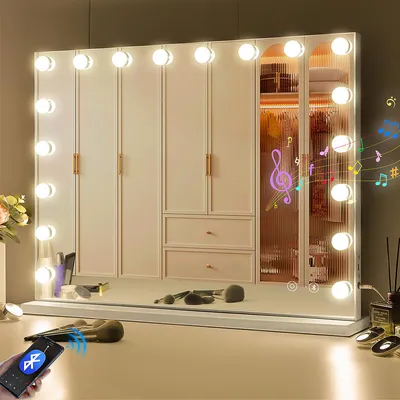 A vanity mirror with lights and makeup brushes on a dresser in front of a wardrobe.