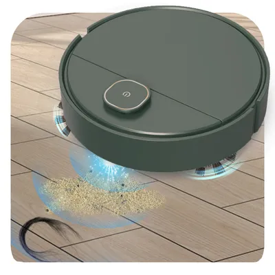 A dark green robot vacuum cleaner is shown cleaning a wooden floor, with dust and hair being sucked up.