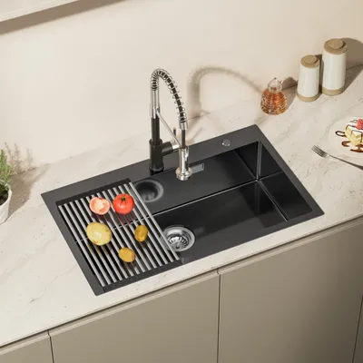 A black-gray kitchen sink with a faucet and a drying rack with vegetables on it, placed on a countertop.