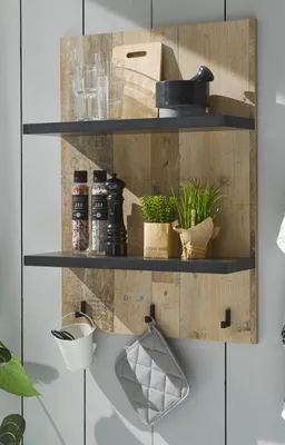 A rustic wooden wall shelf with two shelves, displaying kitchen items like spice jars, a pepper grinder, a plant, and a pot holder.