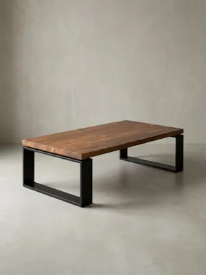 Massiver Couchtisch 115x35x60 cm im Studio. Die braune Sheeshamholz-Platte ruht auf zwei robusten, matt schwarzen Eisenkufen und zeigt ein klares, industrielles Design._#sku_SAFWL5.650#